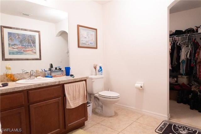 bathroom with a walk in closet, baseboards, toilet, tile patterned floors, and vanity