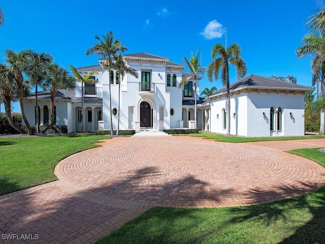 view of front of property featuring curved driveway, a front lawn, a balcony, and stucco siding