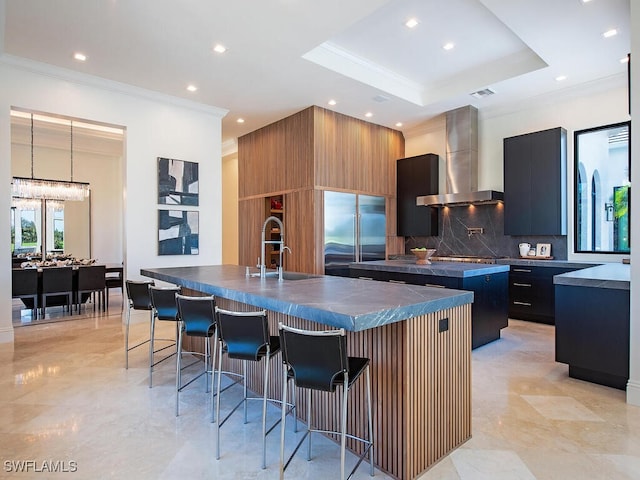 kitchen featuring dark countertops, a large island with sink, stainless steel appliances, and wall chimney exhaust hood