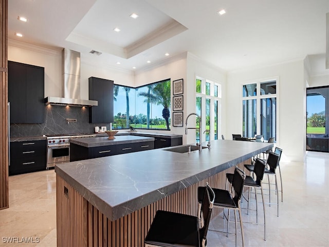 kitchen featuring a sink, a center island with sink, high end range, wall chimney exhaust hood, and dark cabinets