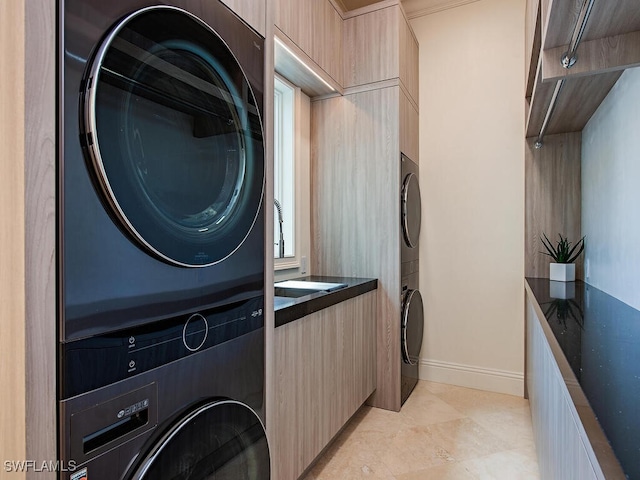 washroom featuring stacked washer / dryer, cabinet space, and baseboards