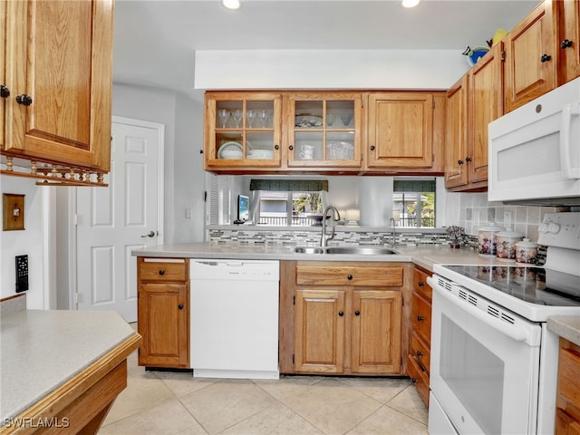 kitchen featuring white appliances, a sink, decorative backsplash, light countertops, and glass insert cabinets