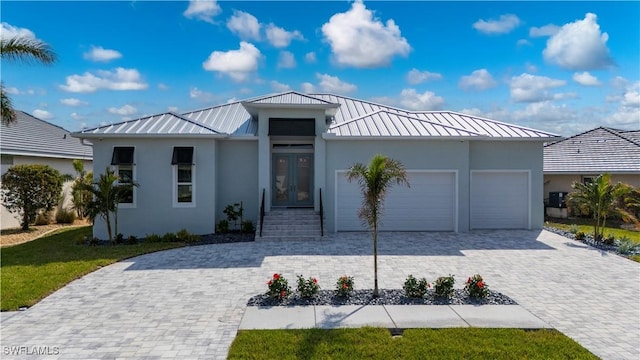 view of front of house with stucco siding, a standing seam roof, decorative driveway, french doors, and a garage