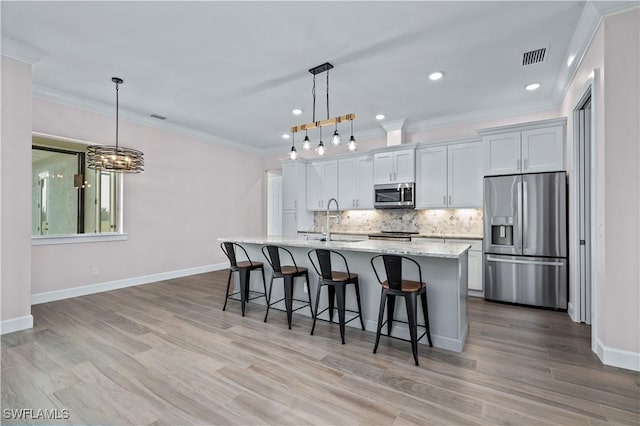 kitchen featuring a center island with sink, a kitchen bar, decorative backsplash, appliances with stainless steel finishes, and a sink