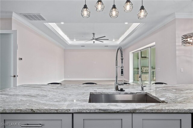 kitchen featuring light stone countertops, visible vents, a tray ceiling, a sink, and crown molding