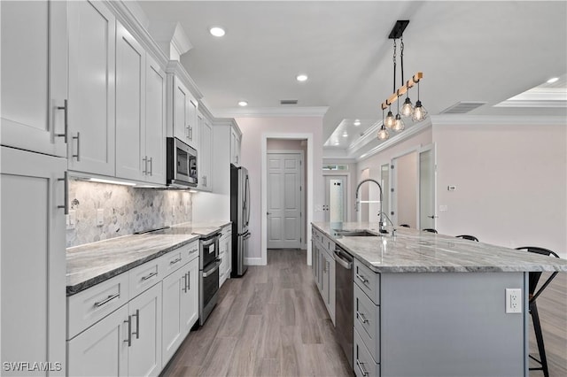 kitchen featuring a center island with sink, a sink, appliances with stainless steel finishes, a kitchen breakfast bar, and backsplash