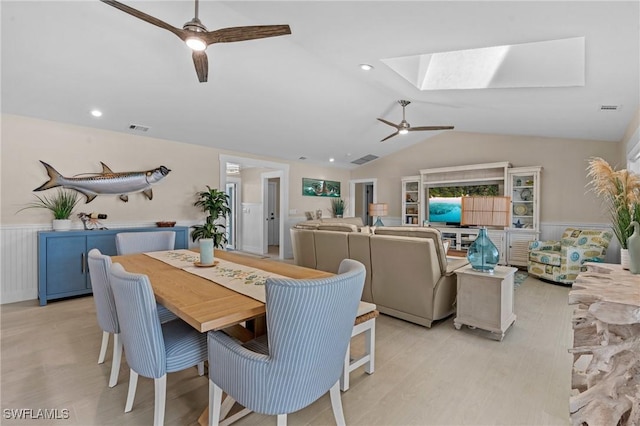 dining room featuring visible vents, vaulted ceiling with skylight, a ceiling fan, and a wainscoted wall