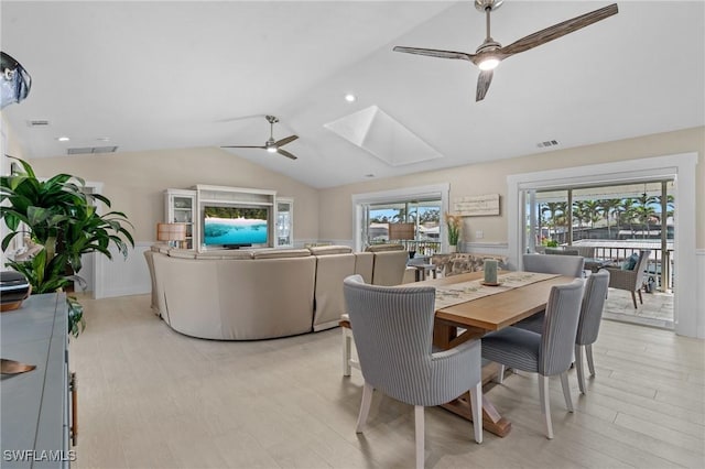 dining area featuring lofted ceiling with skylight, visible vents, light wood finished floors, and ceiling fan