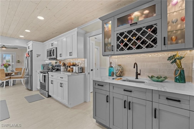 kitchen with light stone counters, a sink, appliances with stainless steel finishes, wooden ceiling, and backsplash