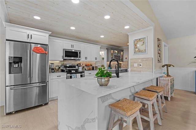 kitchen featuring a kitchen breakfast bar, light wood finished floors, appliances with stainless steel finishes, and wainscoting