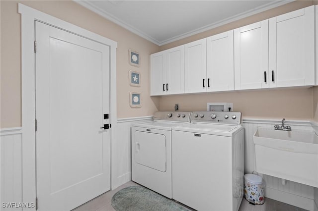 clothes washing area with cabinet space, wainscoting, crown molding, and washing machine and clothes dryer