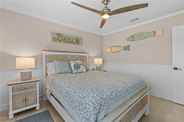 bedroom with wood finished floors, visible vents, and wainscoting