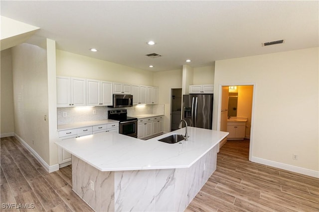 12391 Muddy Creek Ln, Fort Myers, FL 33913 - kitchen with appliances with stainless steel finishes, light wood-style floors, a large island with sink, white cabinets, and tasteful backsplash