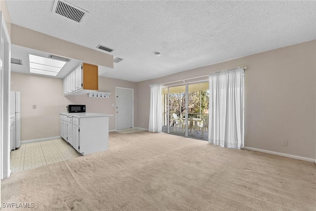 kitchen with open floor plan, visible vents, light colored carpet, and black microwave