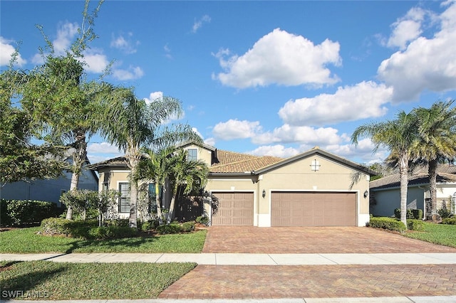 mediterranean / spanish home featuring stucco siding, decorative driveway, an attached garage, and a tile roof