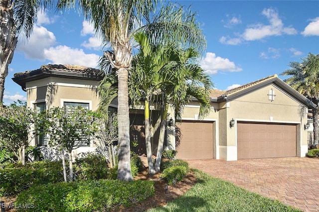 mediterranean / spanish home with a tile roof, decorative driveway, a garage, and stucco siding