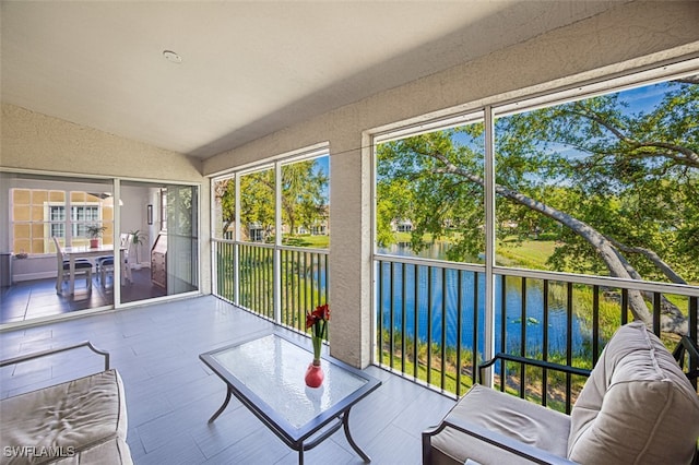 sunroom featuring a water view, a textured wall, a wealth of natural light, and lofted ceiling