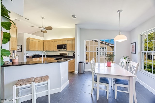 kitchen featuring dark countertops, light brown cabinets, vaulted ceiling, decorative backsplash, and appliances with stainless steel finishes