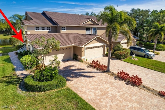 view of front of home with a front yard, stucco siding, a garage, a tile roof, and decorative driveway