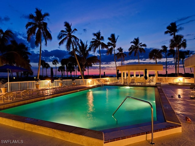 pool at dusk with a patio, a community pool, and fence