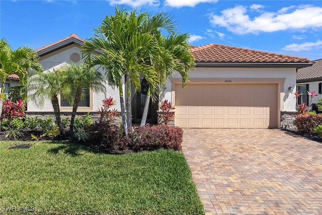 mediterranean / spanish house with a front lawn, a tile roof, stucco siding, decorative driveway, and an attached garage