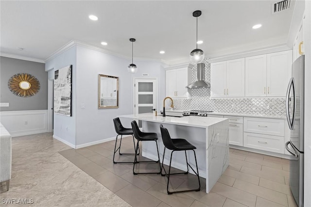 kitchen with visible vents, freestanding refrigerator, a sink, crown molding, and wall chimney exhaust hood