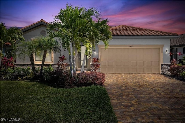 mediterranean / spanish home featuring stucco siding, decorative driveway, a garage, and a tiled roof