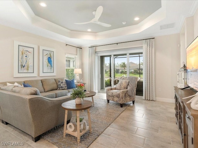 living room with a raised ceiling, a ceiling fan, baseboards, and ornamental molding