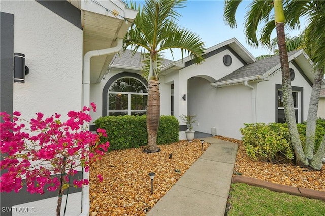 entrance to property with a shingled roof and stucco siding