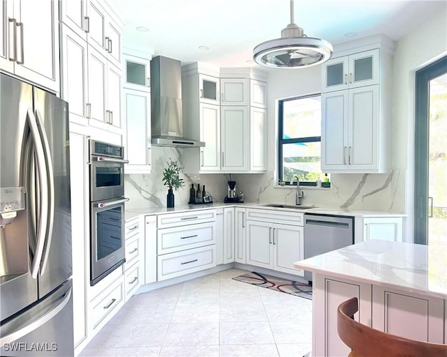 kitchen featuring a sink, light stone counters, tasteful backsplash, appliances with stainless steel finishes, and wall chimney exhaust hood