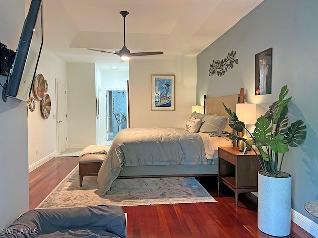 bedroom with a ceiling fan, a raised ceiling, wood finished floors, and baseboards