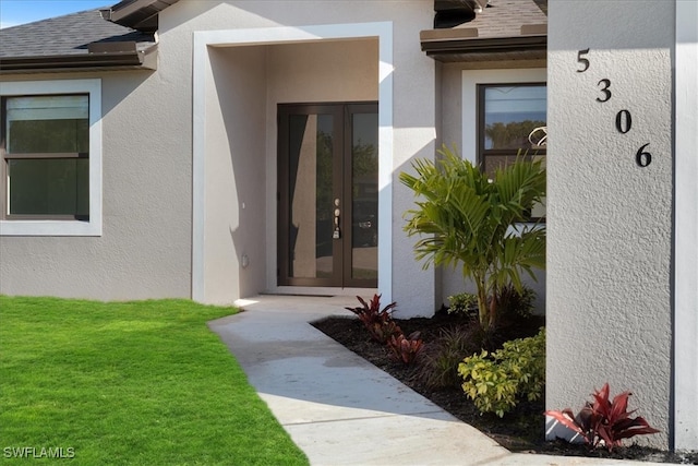 doorway to property featuring stucco siding, a yard, and a shingled roof