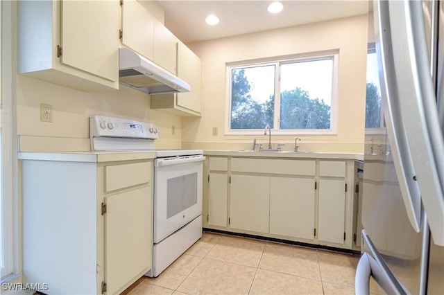 kitchen featuring electric range, under cabinet range hood, a sink, freestanding refrigerator, and light tile patterned floors