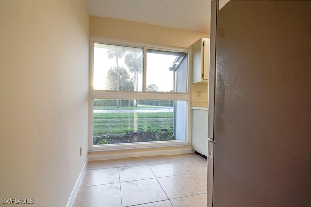 empty room with light tile patterned floors, plenty of natural light, and baseboards