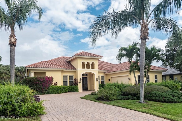 mediterranean / spanish house with stucco siding, a tiled roof, decorative driveway, and a garage