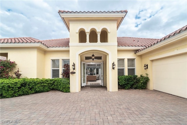 property entrance with stucco siding, decorative driveway, a garage, and a tiled roof