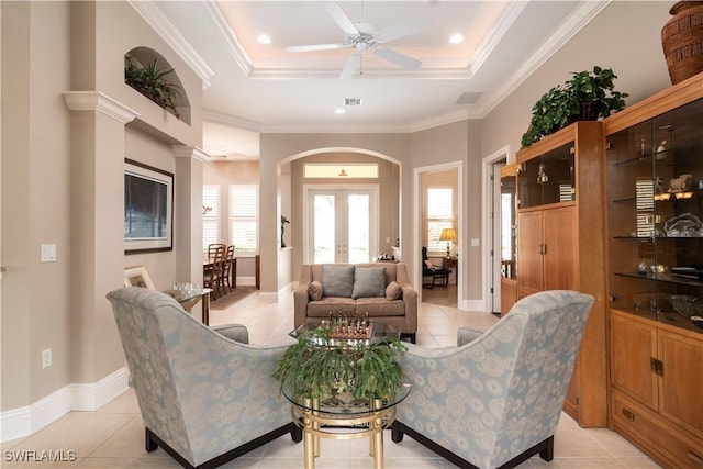 living room featuring light tile patterned floors, a tray ceiling, arched walkways, and ornamental molding