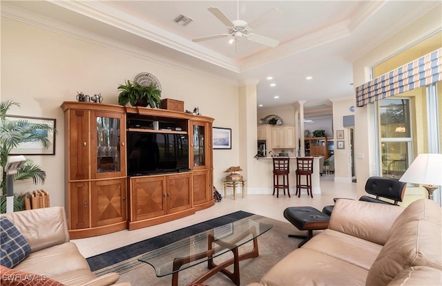 living room with a raised ceiling, ornamental molding, visible vents, and ceiling fan