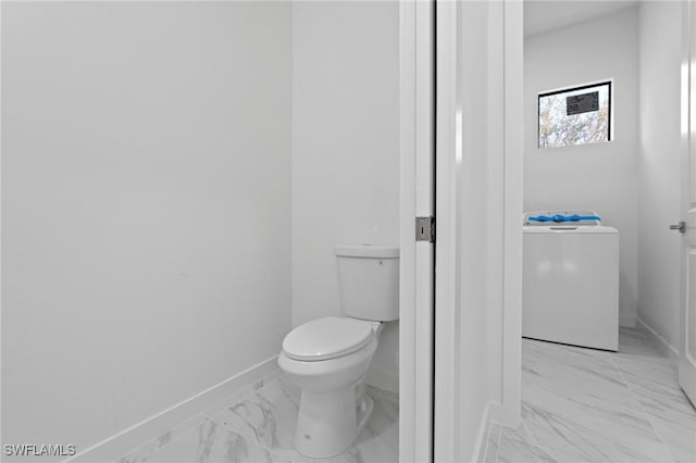 bathroom with washer / dryer, toilet, baseboards, and marble finish floor