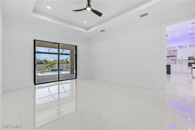 empty room with a ceiling fan, visible vents, recessed lighting, a raised ceiling, and marble finish floor