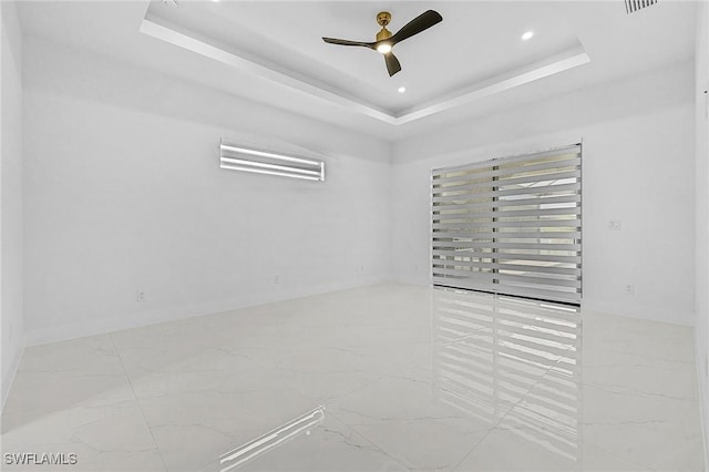 empty room featuring a raised ceiling, a ceiling fan, and marble finish floor