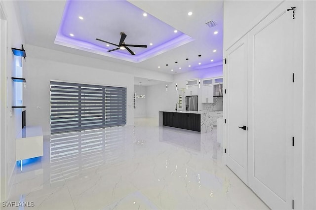 unfurnished living room featuring a tray ceiling, visible vents, marble finish floor, and ceiling fan