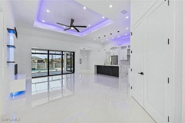 interior space featuring a tray ceiling, a ceiling fan, visible vents, and marble finish floor