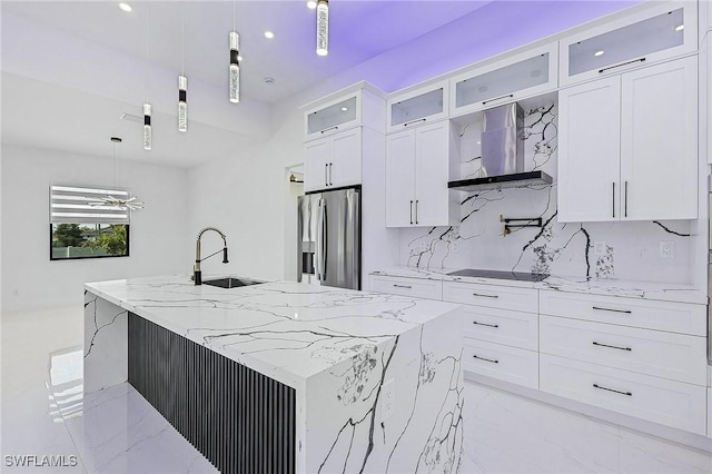 kitchen featuring an island with sink, a sink, white cabinetry, wall chimney exhaust hood, and stainless steel fridge