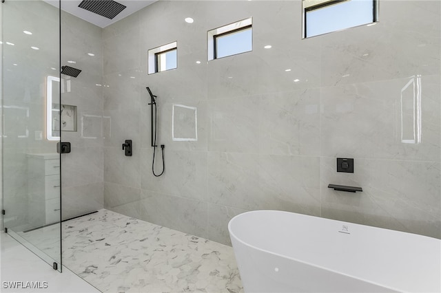 bathroom with a soaking tub, marble finish floor, tiled shower, and tile walls