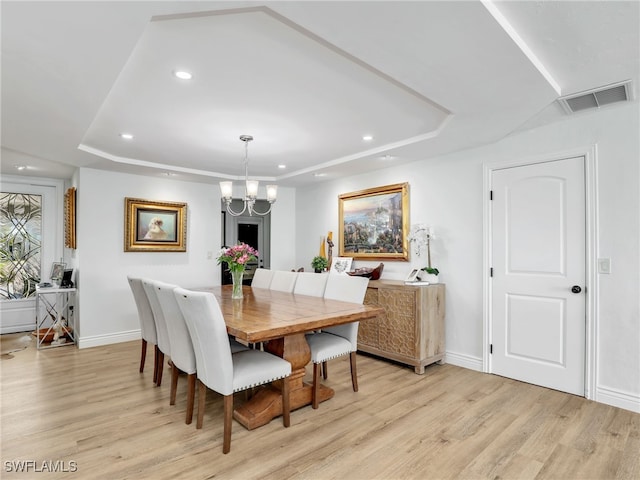 dining area with a tray ceiling, visible vents, and light wood finished floors