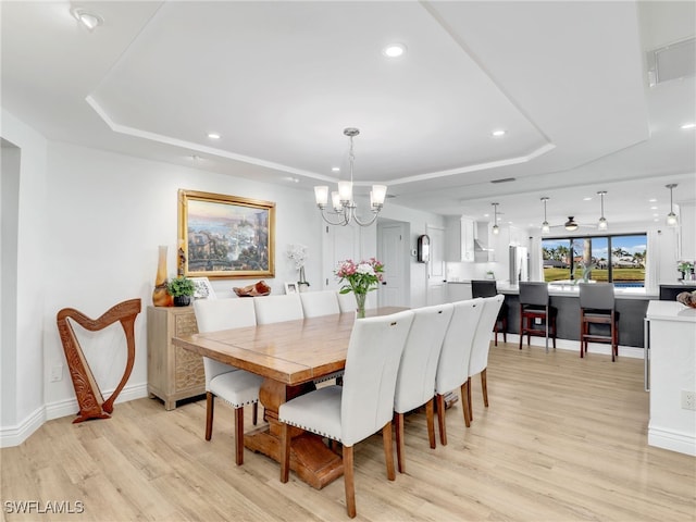 dining room with a raised ceiling, an inviting chandelier, and light wood-style flooring