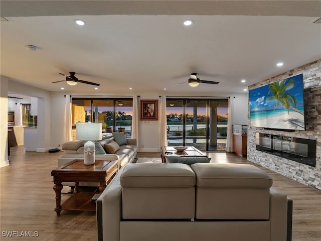 living room with a stone fireplace, recessed lighting, wood finished floors, and ceiling fan