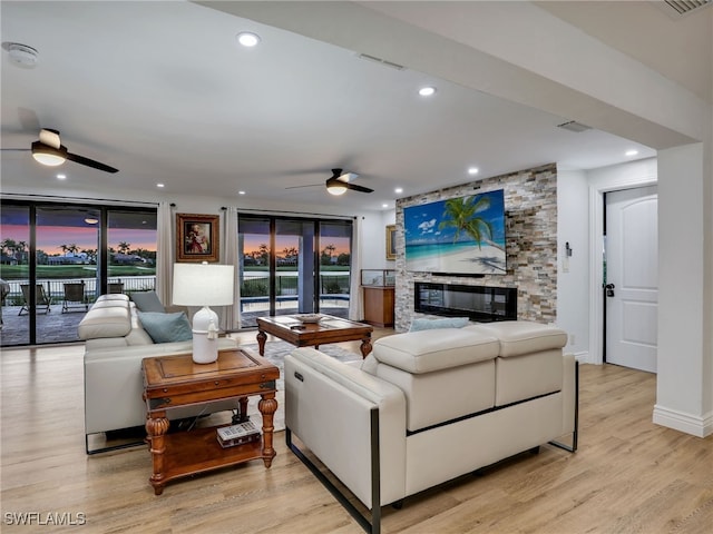 living room with light wood-type flooring, visible vents, a ceiling fan, recessed lighting, and a stone fireplace