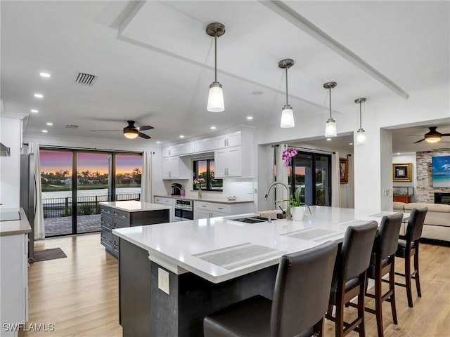 kitchen featuring visible vents, ceiling fan, a large island, white cabinets, and light wood-type flooring